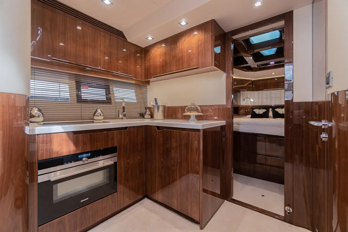 Modern yacht interior showcasing a sleek kitchen with wooden cabinetry, countertop, and doorway leading to a stylish bedroom.